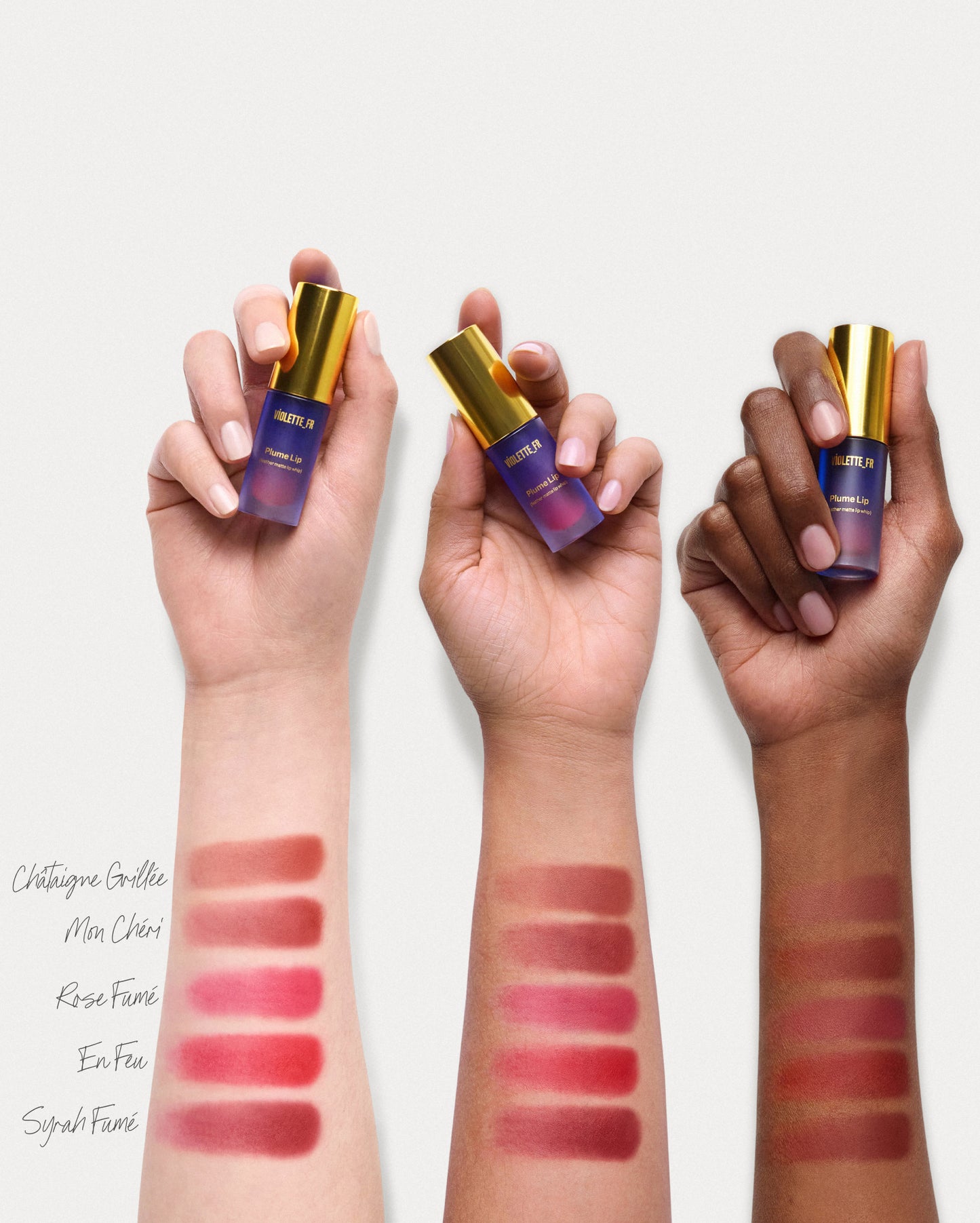 VIOLETTE_FR Plume Lip feather-matte lip whip products held by hands of light, medium, and deep skin tones, with swatches of Châtaigne Grillée, Mon Chéri, Rose Fumé, En Feu, and Syrah Fumé shown on corresponding forearms. - Plume Essentials Trio
