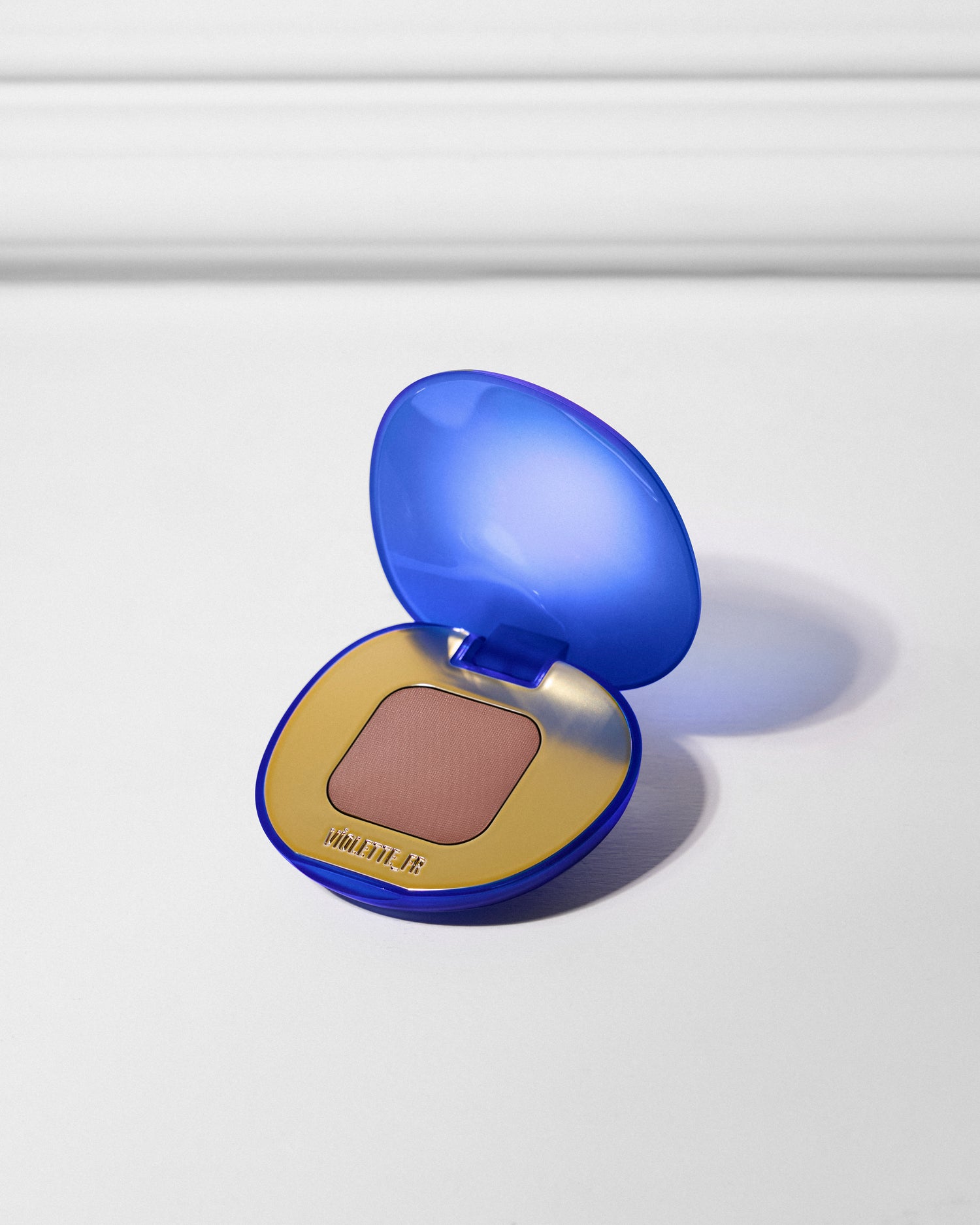 VIOLETTE_FR is embossed on the gold interior of an open vibrant blue compact, revealing a square pan of warm, medium brown blush or bronzer.