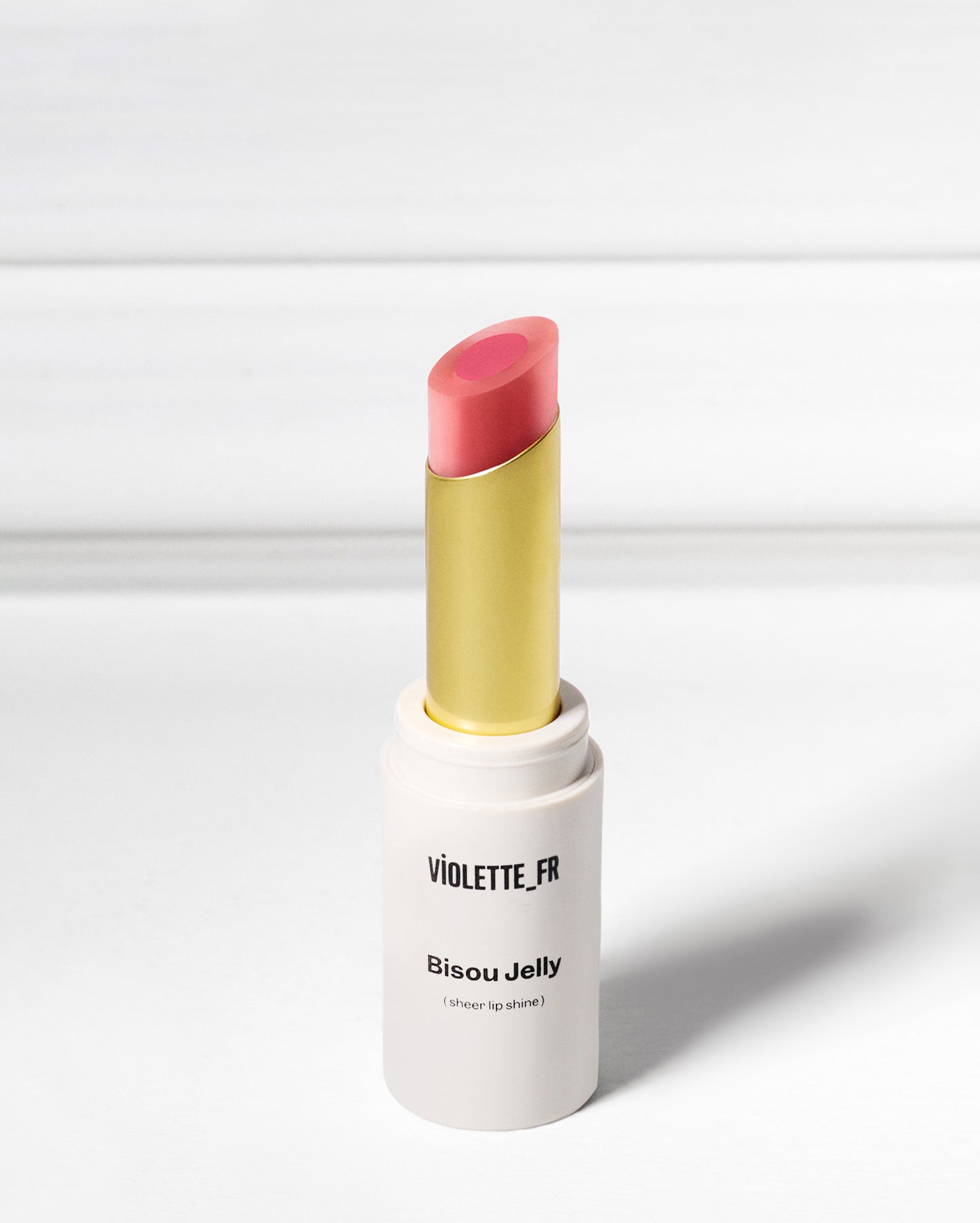 Violette_FR Bisou Jelly (sheer lip shine) in a two-toned pink shade, with a gold inner tube, standing upright.