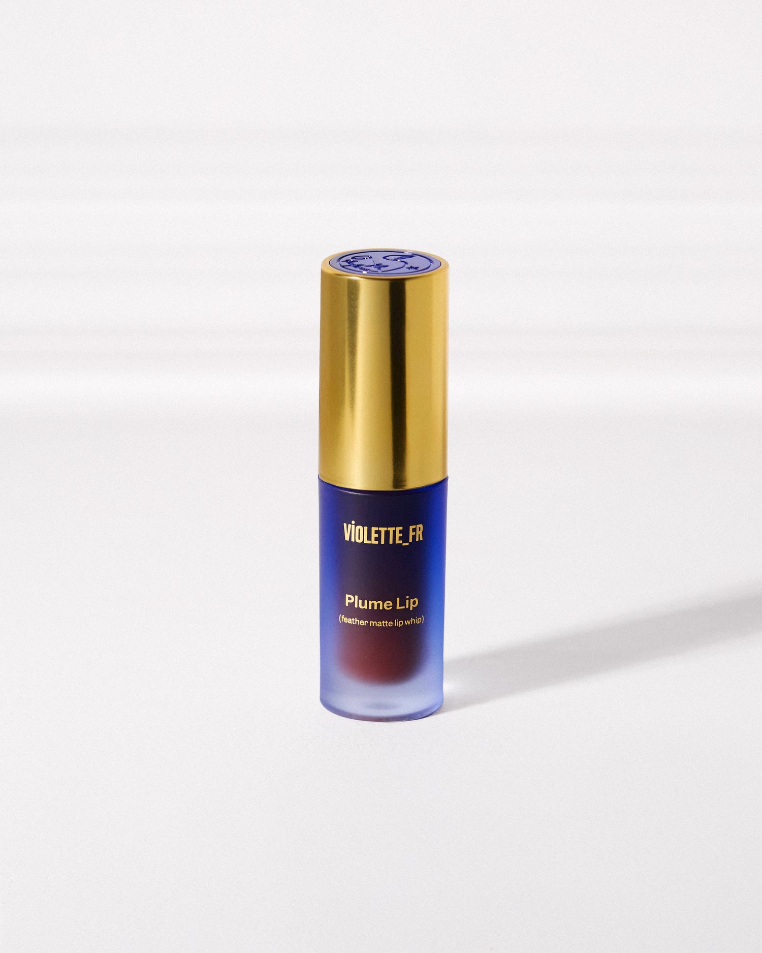 Violette_FR Plume Lip (feather matte lip whip) in a frosted blue-purple bottle with a gold cap, showing a deep red lip whip inside.