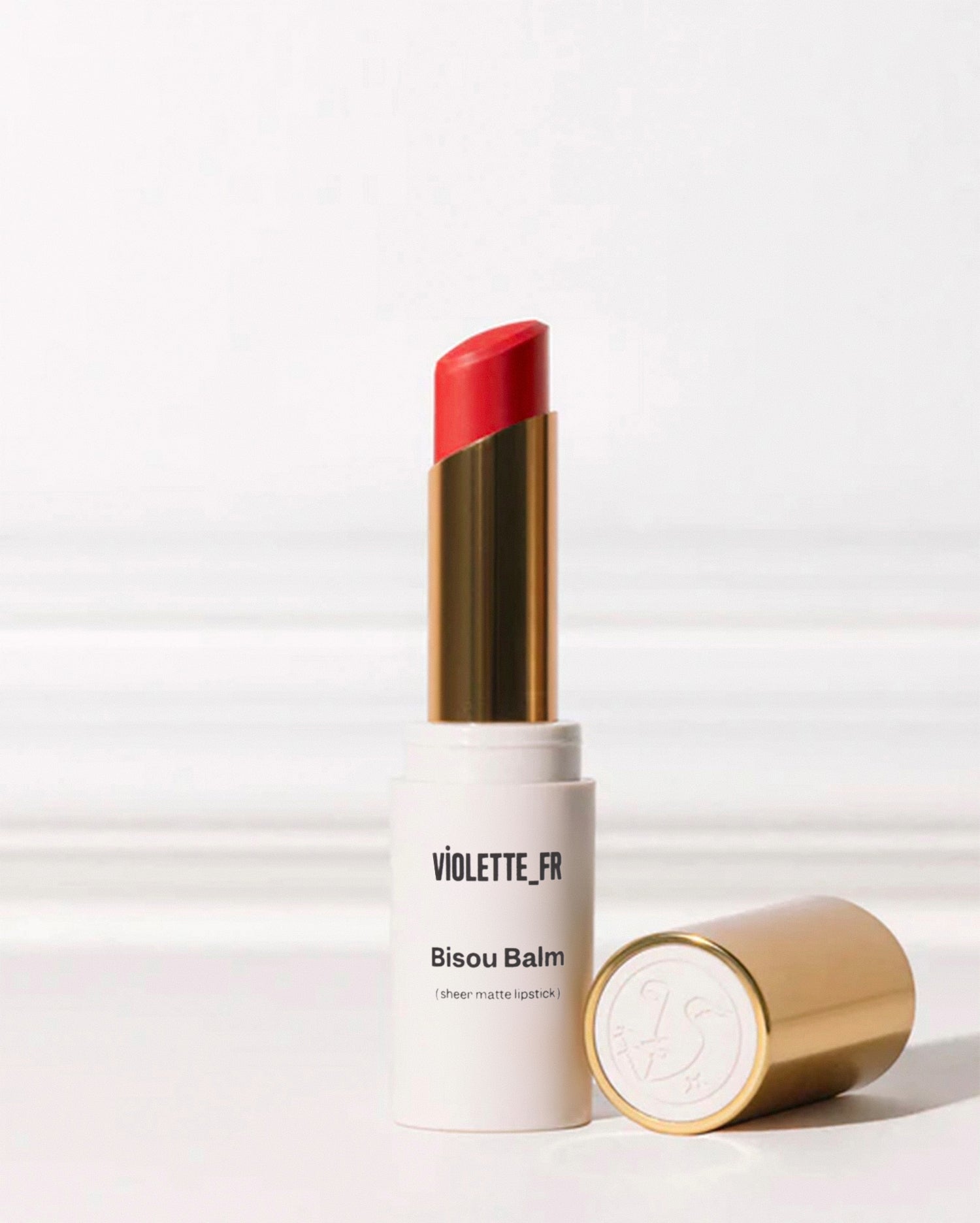 Bisou Balm - Bêtise - Bisou Balm (sheer matte lipstick) by VIOLETTE_FR. A red lipstick is extended from its white tube, with the gold cap featuring a 'VF' logo lying next to it. - Image 101 of 101