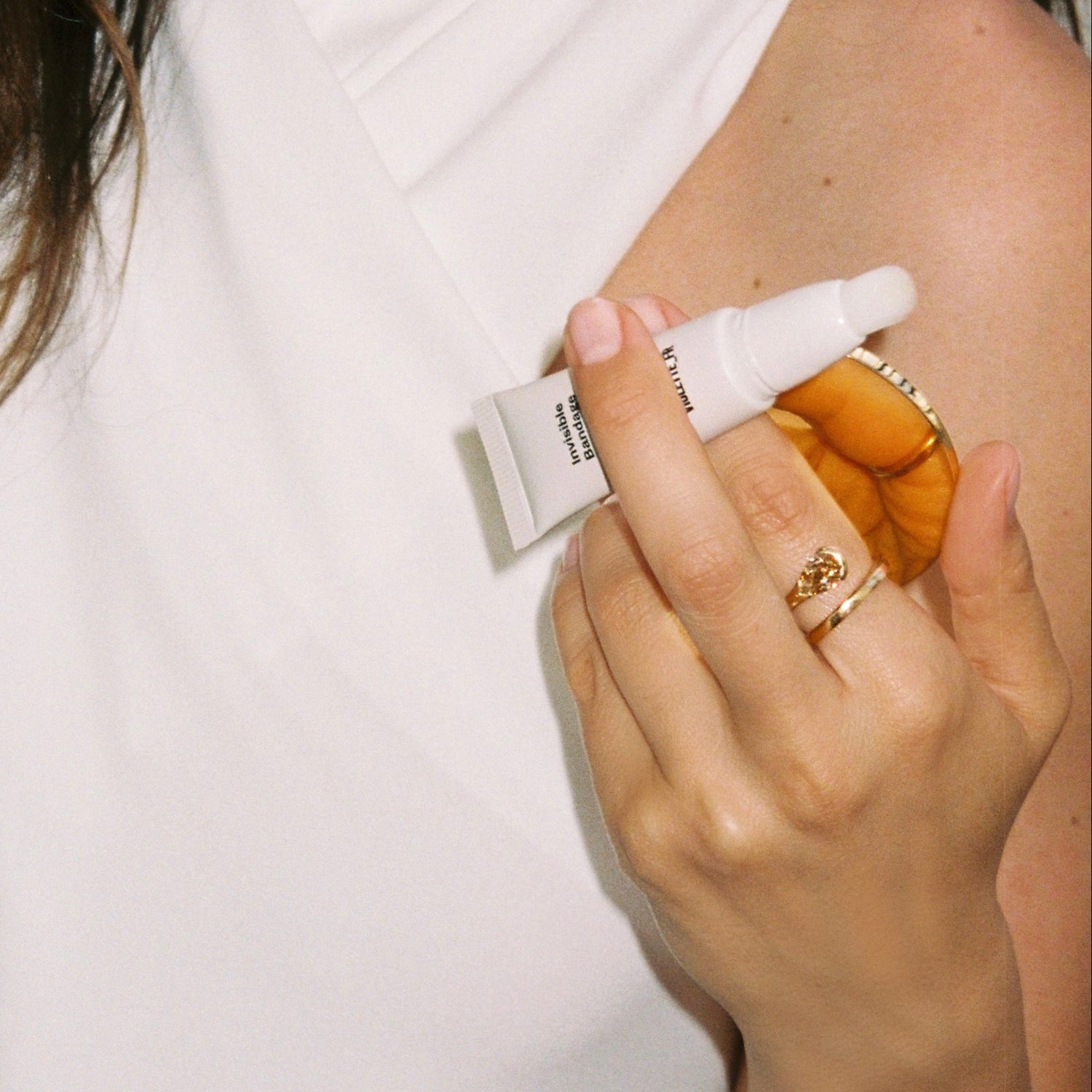 hand holding the invisible bandage tube with the cap off and holding a gold mirror white shirt in the background