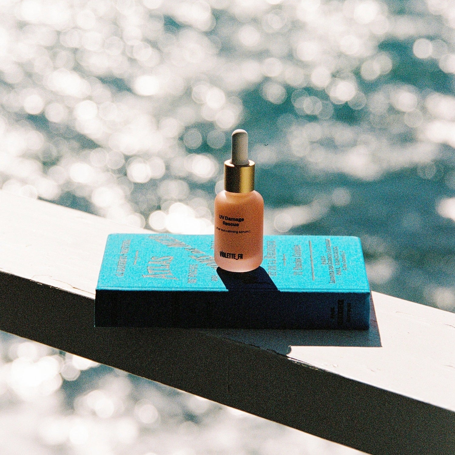 UV damage resuce serum bottle on top of a blue book that is resting on top of a ledge with the ocean in the background