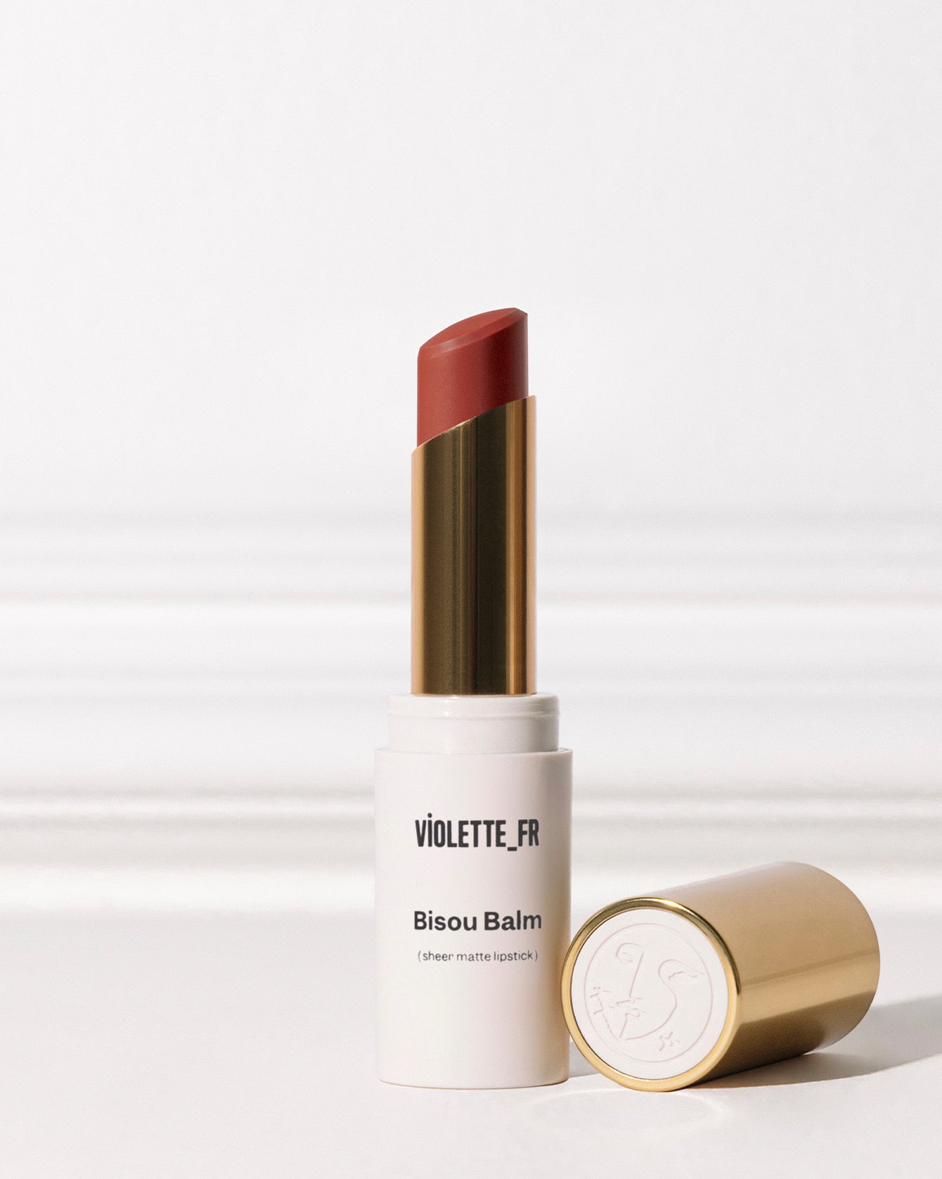 Bisou Balm - Bêtise - Bisou Balm (sheer matte lipstick) by VIOLETTE_FR, a reddish-brown shade, shown in its white and gold tube with the cap off. - Image 21 of 21