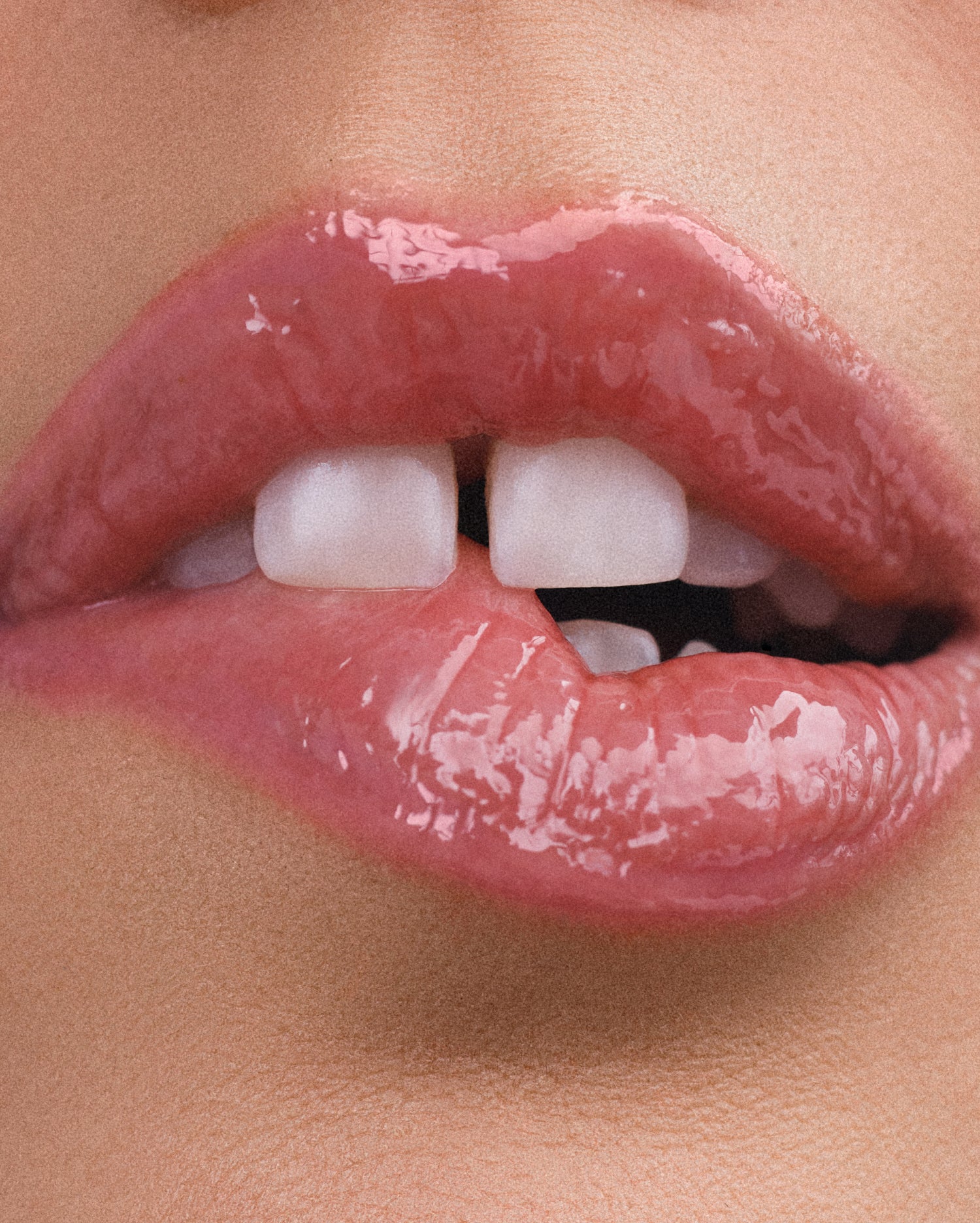 A close-up of pink, glossy lips. One side of the bottom lip is bitten and the other is slightly parted.