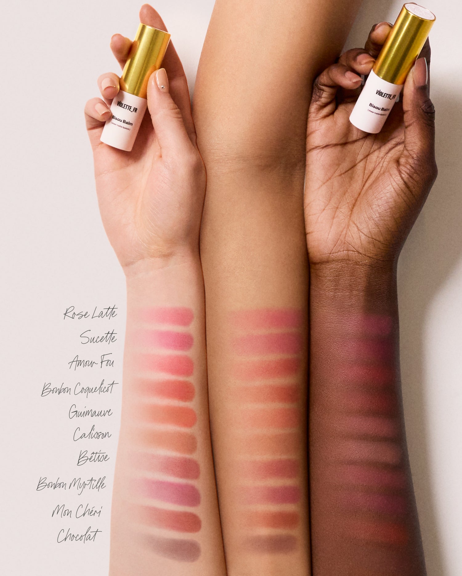 Bisou Balm - Calisson - Three forearms of light, medium, and deep skin tones hold a Bisou Balm (sheer matte lipstick) from VIOLETTE_FR. Each arm displays 10 swatches of shades: Rose Latte, Sucette, Amour Fou, Bonbon Coquelicot, Guimauve, Calisson, Bêtise, Bonbon Myrtille, Mon Chéri, and Chocolat. - Image 32 of 32