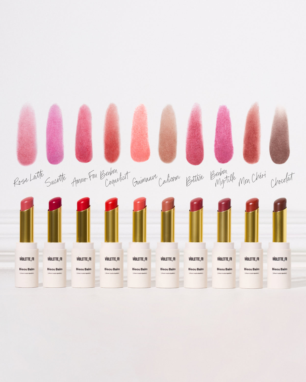 Bisou Balm - Calisson - Ten VIOLETTE_FR Bisou Balm sheer matte lipsticks, including shades Rose Latte, Sucette, Amour Fou, Bonbon Coquelicot, Guimauve, Calisson, Bêtise, Bonbon Myrtille, Mon Chéri, and Chocolat, are shown with their swatches on a white background. The lipsticks are in white and gold tubes, and the shades range from light pinks to deep berry to cool brown tones. - Image 33 of 33