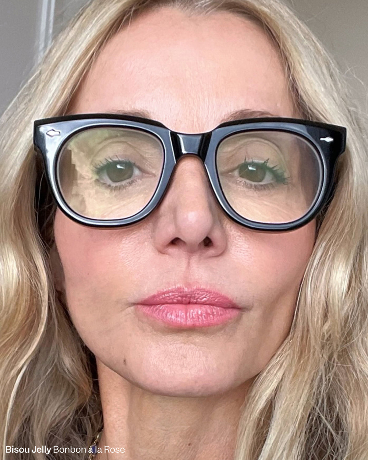 Bisou-Bisou Lip Duo - Bonbon à la Rose. A woman with light to medium skin tone, blonde wavy hair, and black-framed glasses wears the vibrant pink lipstick shade. - Image 5 of 16
