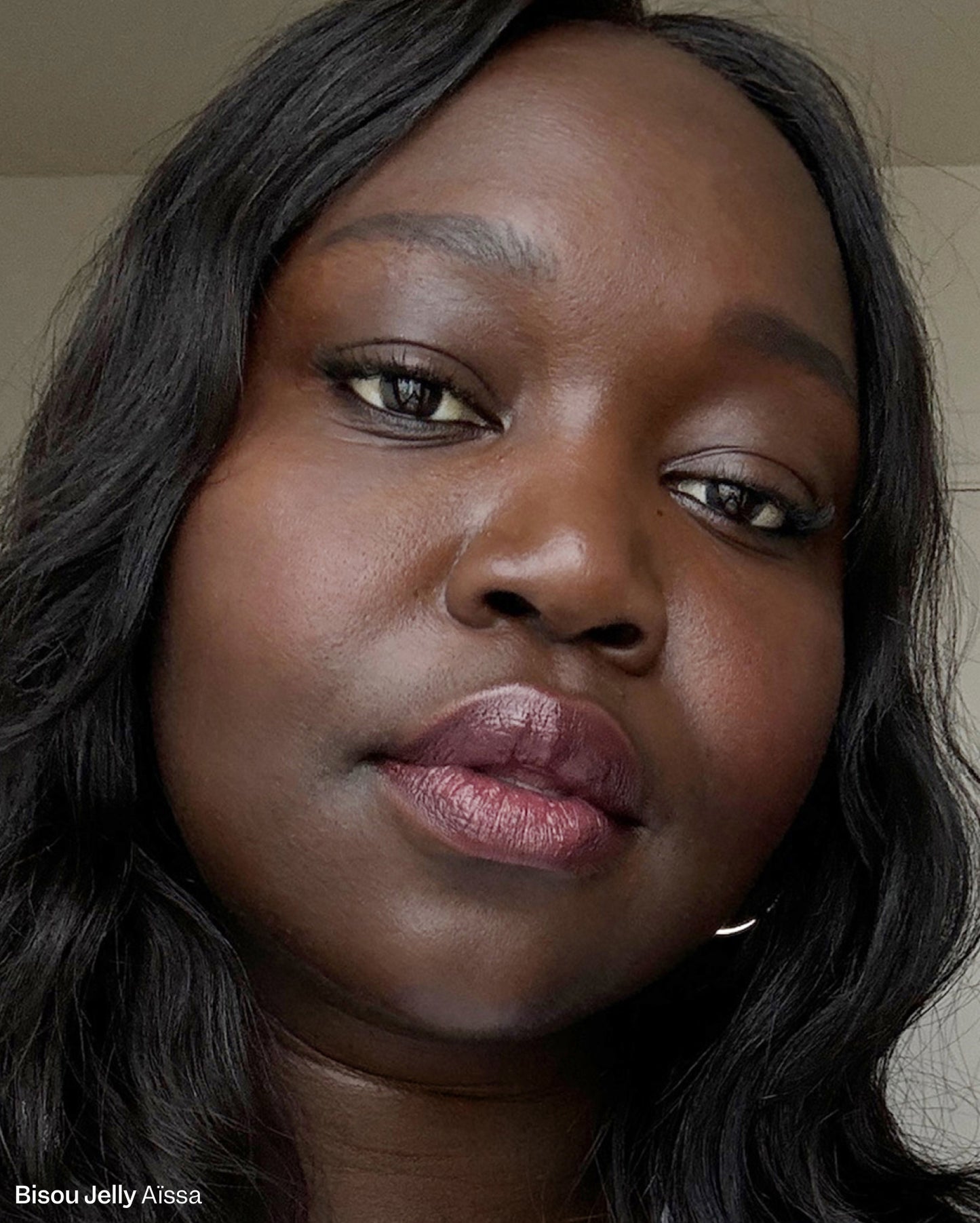 Bisou Jelly Aïssa. Close-up of a woman with deep skin tone wearing a glossy plum-colored lip product. - Bisou-Bisou Lip Duo
