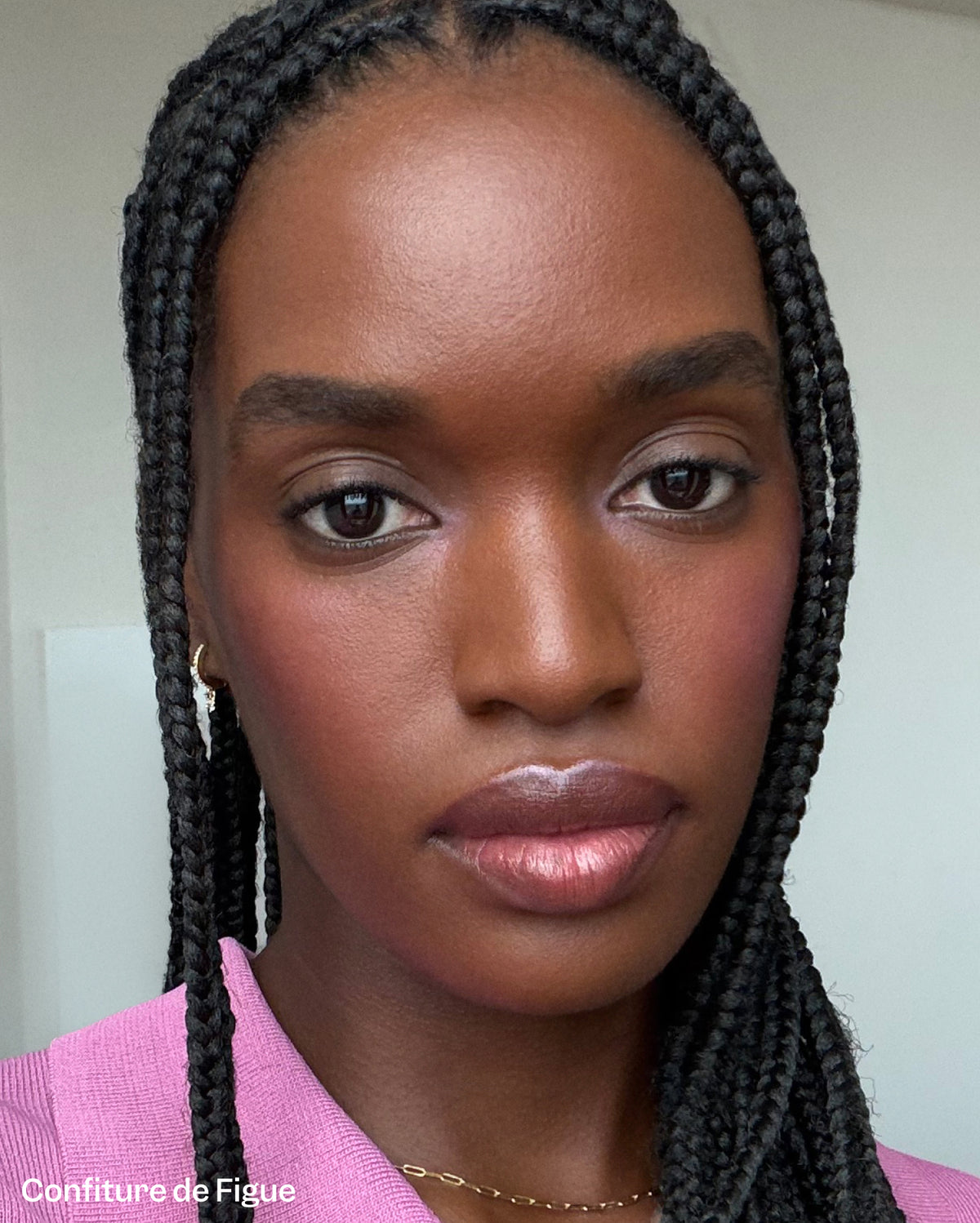A close-up of a person with dark, braided hair and warm brown eyes, and deep skin tone. She has soft, naturally defined nude lips, which catch the light and create a hydrated finish. - Bisou Jelly