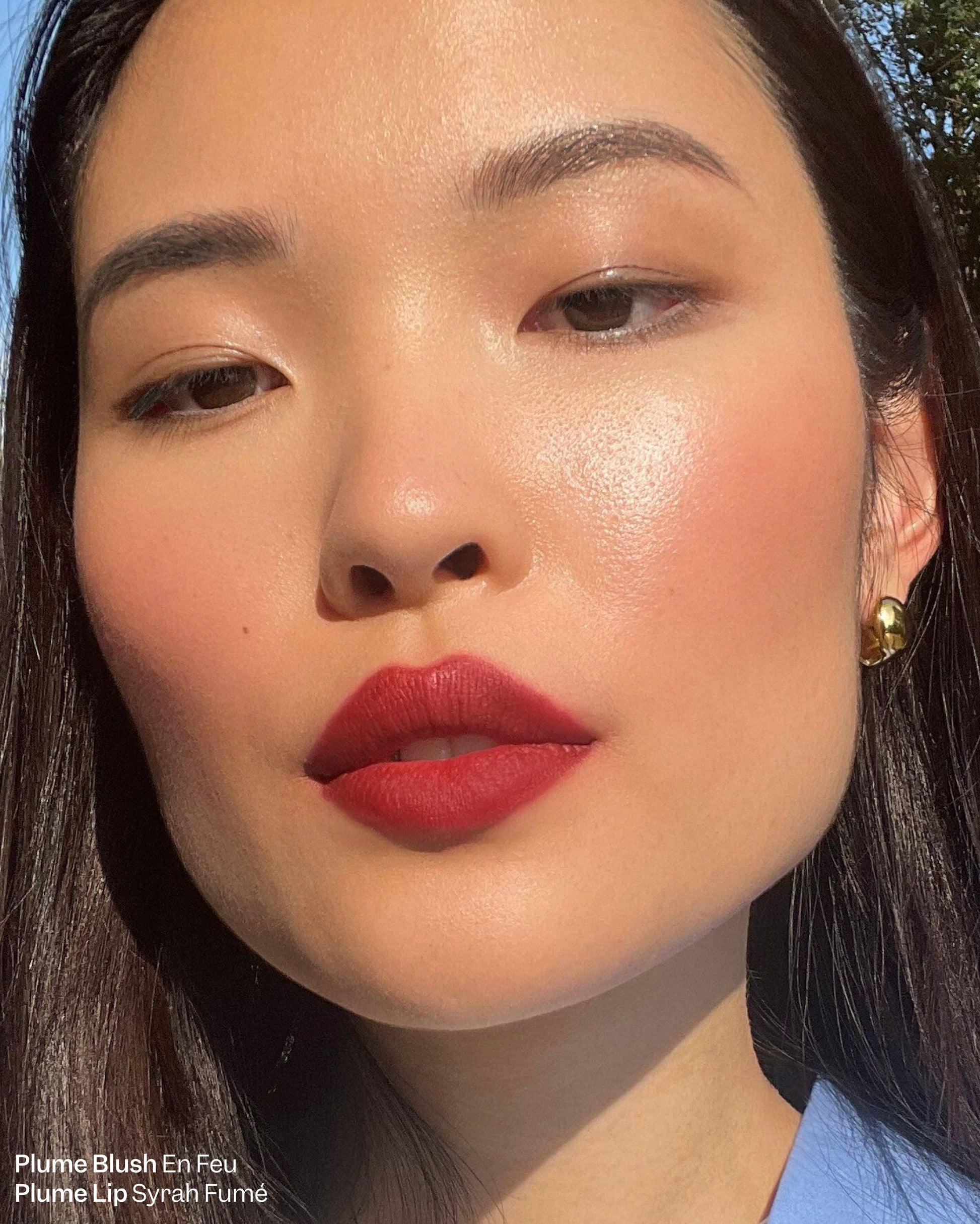 Plume Essentials Trio - Plume Blush En Feu and Plume Lip Syrah Fume. Up close shot of woman with dark brown hair wearing bold red lipstick and blush - Image 3 of 17