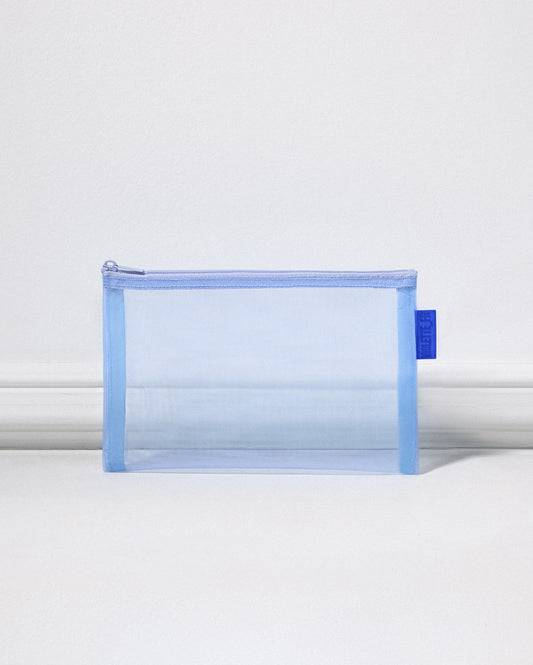A translucent, light blue mesh pouch with a royal blue tag on the side stands in front of a white background. - VIOLETTE_FR Pouch in Bleu Clair