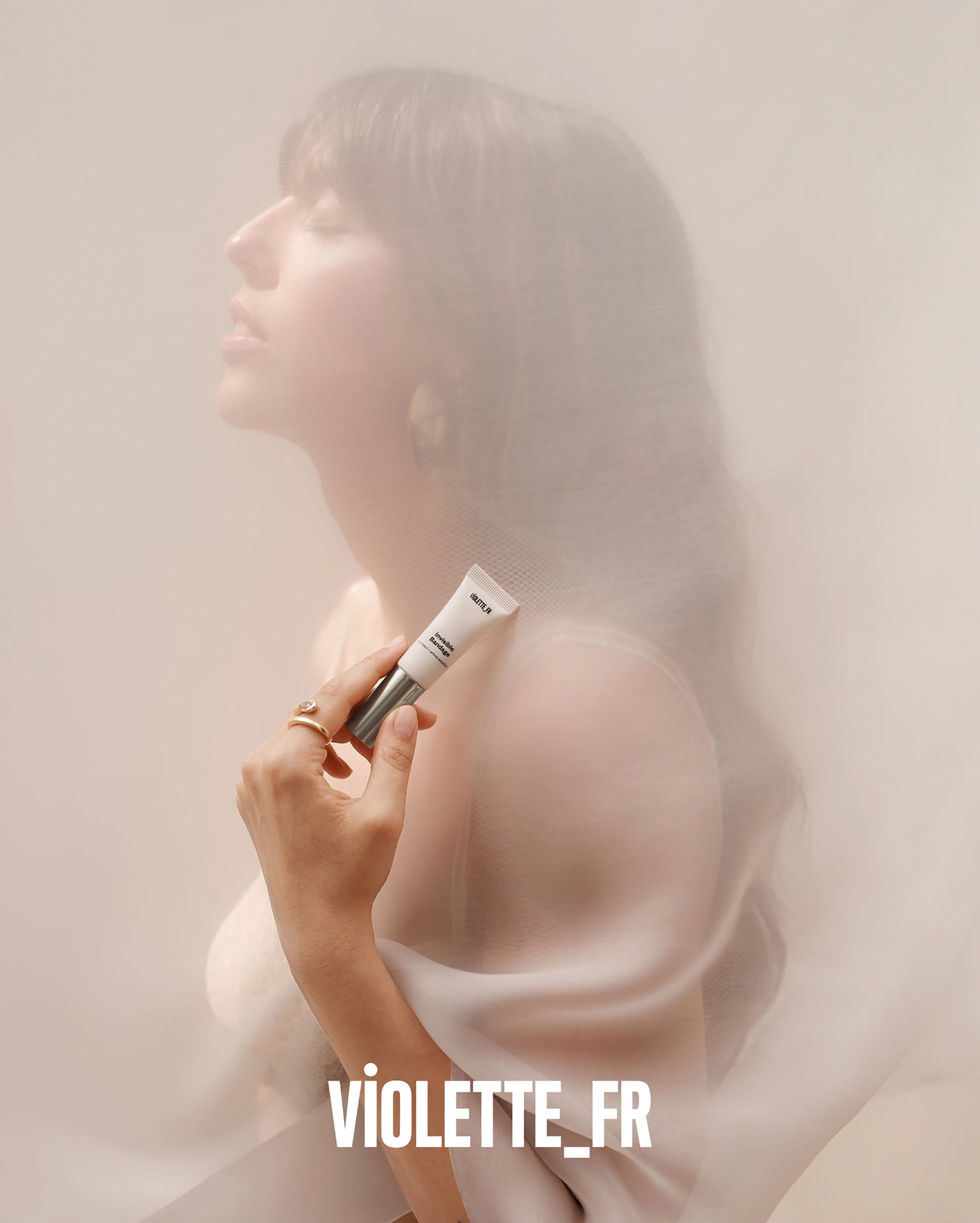 Invisible Bandage - The product tube, labeled "Invisible Bandage" and "VIOLETTE_FR", is held by a light-skinned woman whose face is softly veiled by sheer fabric. "VIOLETTE_FR" is also at the bottom. - Image 11 of 14