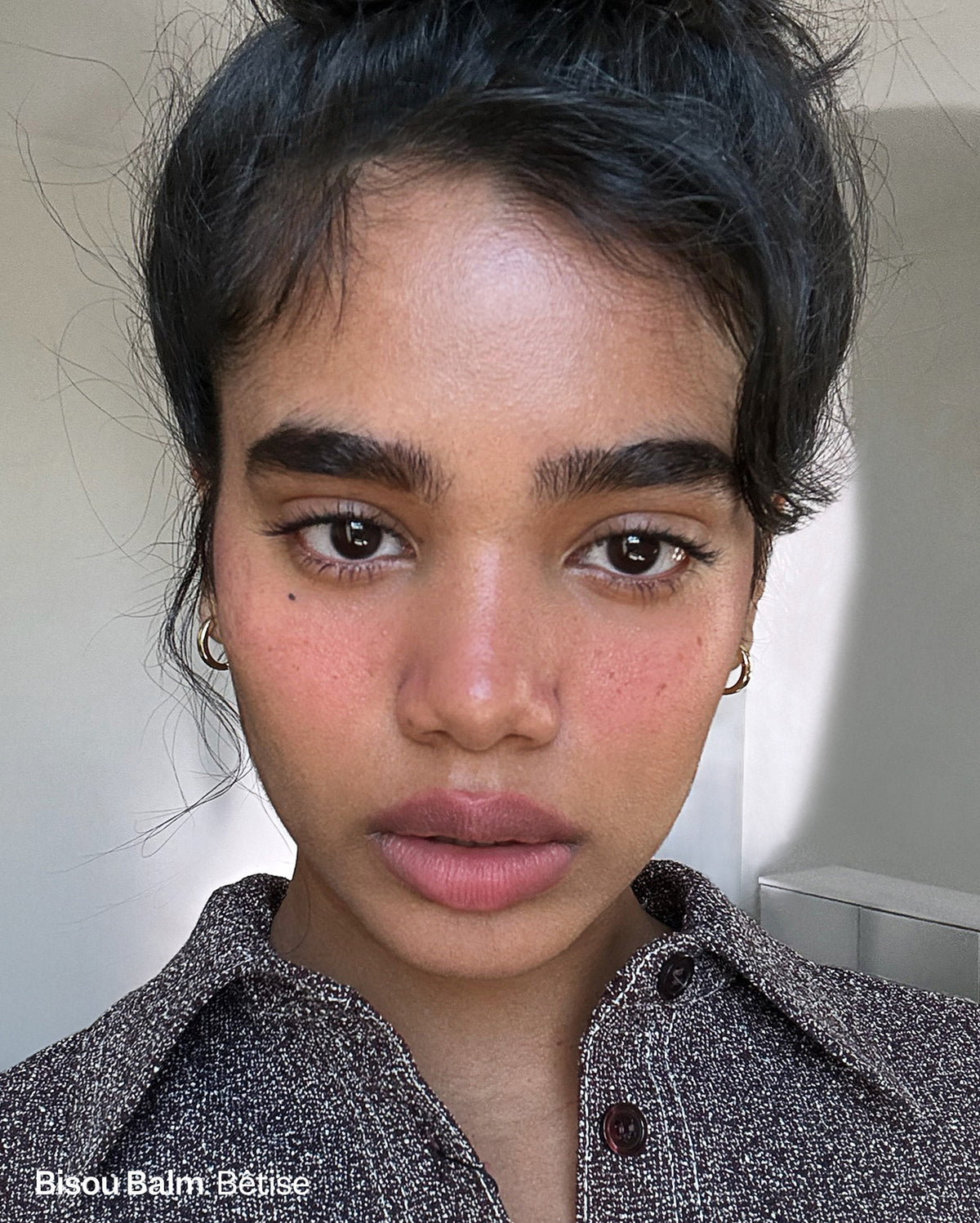 Bisou Balm Bêtise. Close-up of a person with medium skin tone, wearing a rosy blush on cheeks and a natural pink lip color. - Duo Plume Lip & Bisou Balm