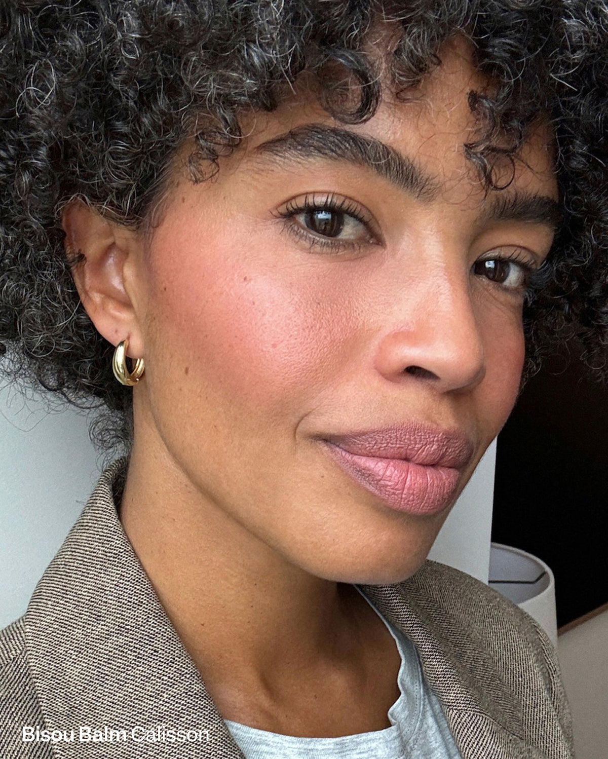 Bisou Balm in Calisson: A model with medium-deep skin tone wears a matte dusty rose lipstick and peachy-pink blush. - Duo Plume Lip & Bisou Balm