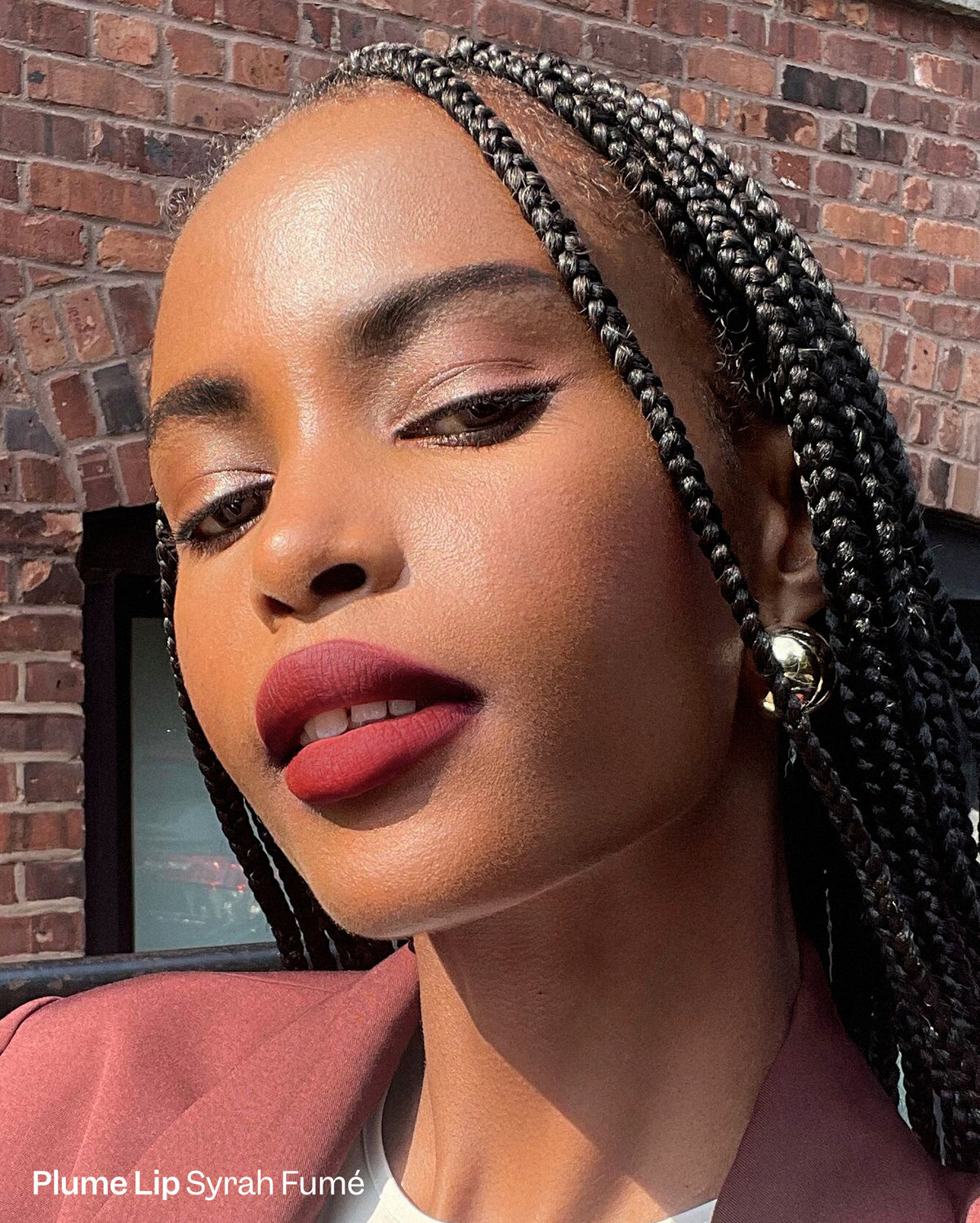 Duo Plume Lip & Bisou Balm - Plume Lip: Syrah Fumé. A woman with deep skin tone wears a matte deep red lipstick and shimmery pink eyeshadow, with black box braids. - Image 3 of 15