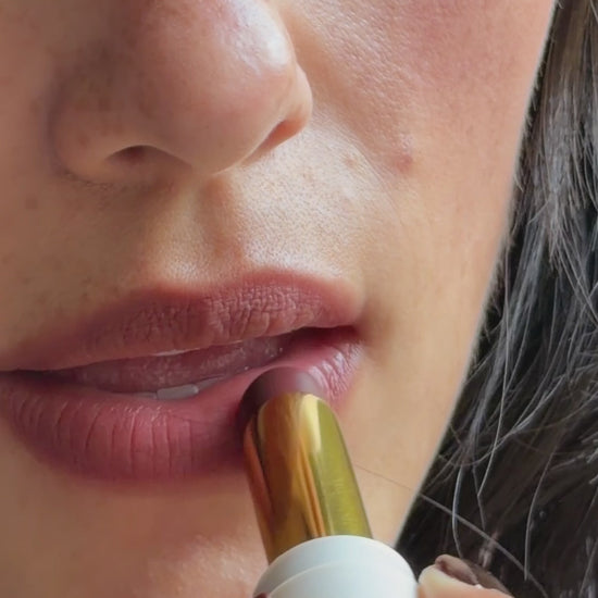 Sheer matte balm swiped from the gold lipstick bullet across the lips, shown on medium skin tone. - Bisou Balm
