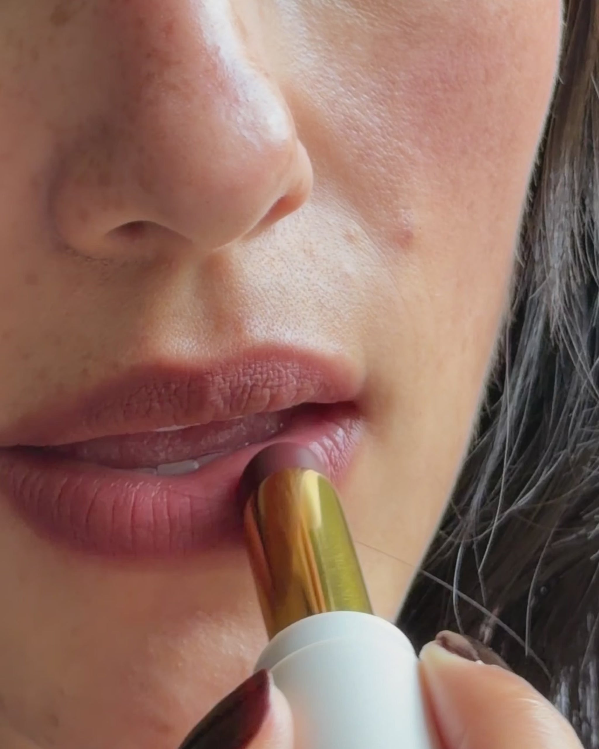 Sheer matte balm swiped from the gold lipstick bullet across the lips, shown on medium skin tone. 