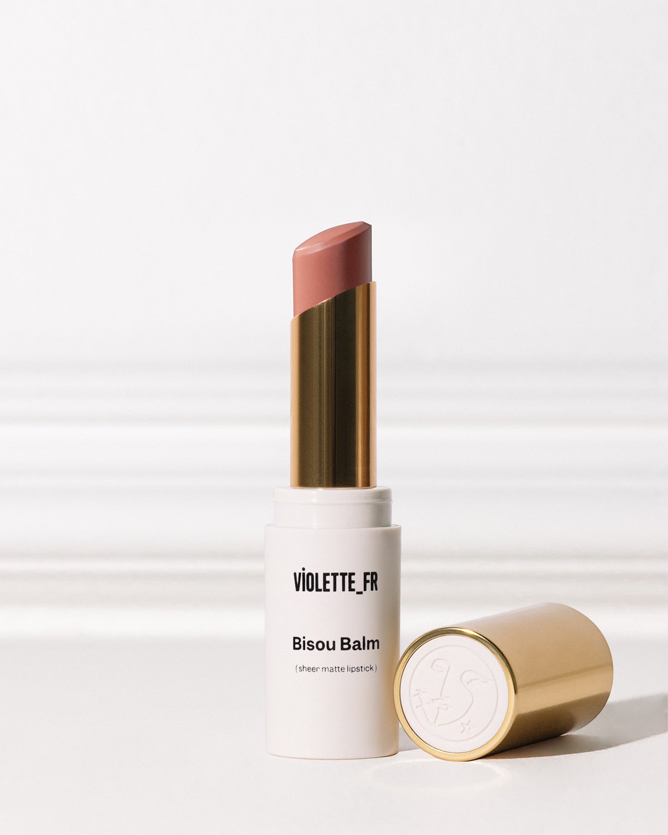 Bisou Balm - Bêtise - Bisou Balm (sheer matte lipstick) by VIOLETTE_FR, shown in an open white and gold tube with a muted pinkish-brown shade, with its gold cap lying next to it. - Image 158 of 158